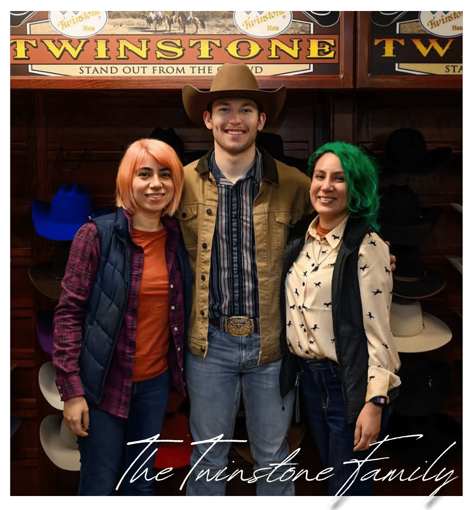 Tristan Roberson posing with two women in front of the Twinstone Hats display wall, all smiling and dressed in Western wear.